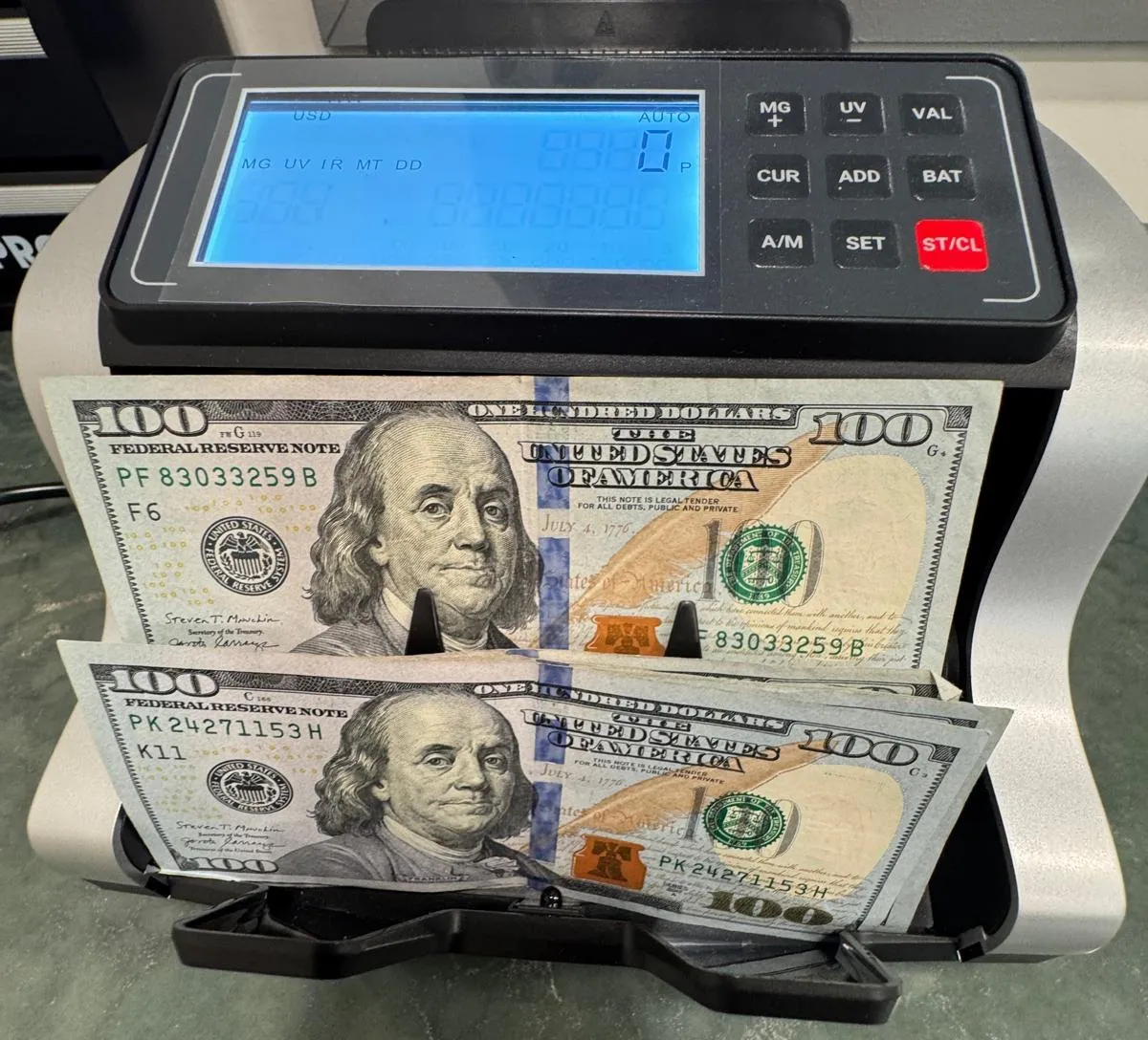 A bill counter on the counter with hundred-dollar notes in its tray
