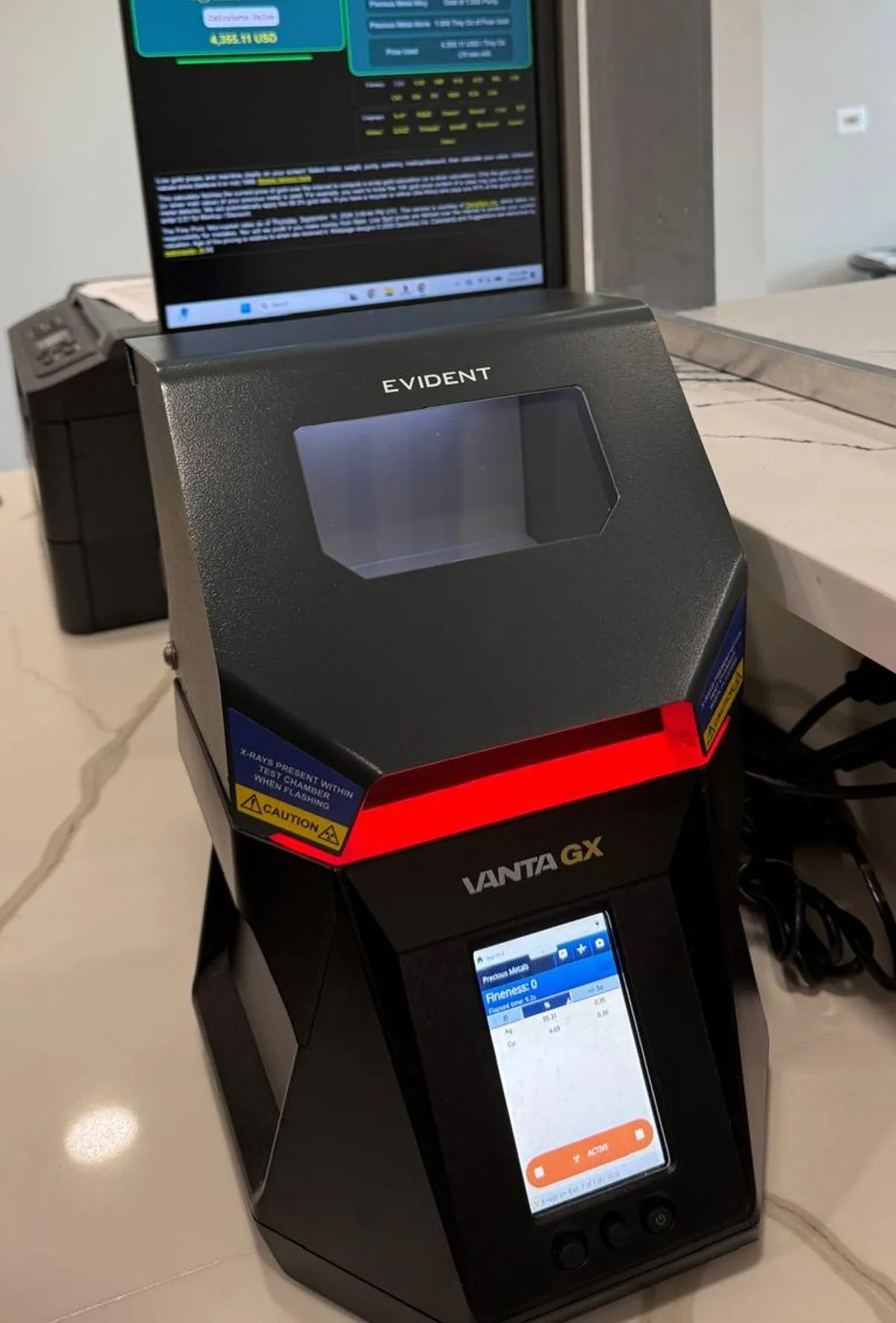 The Evident Vanta GX XRF analyzer on the marble counter, with the price screen behind it